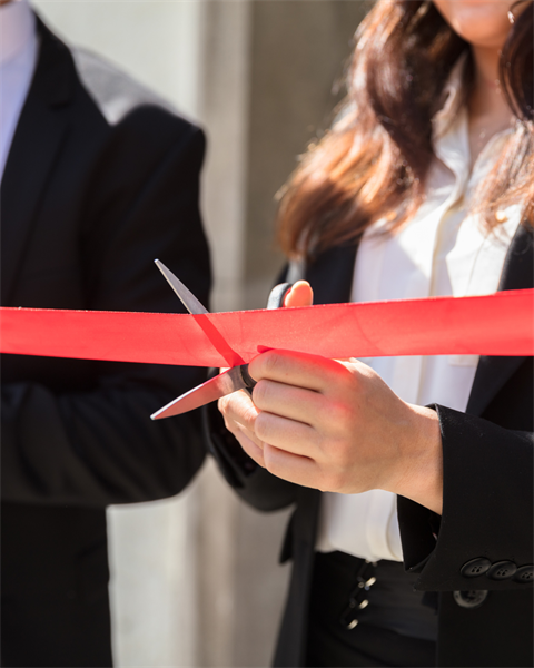 Stock image of a person holding scissors and cutting a red ribbon. 