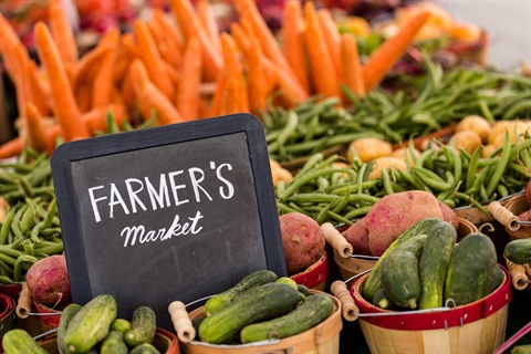 Farmer's Market sign surrounded by buckets of zucchini, red potatoes, green beans and carrots. 