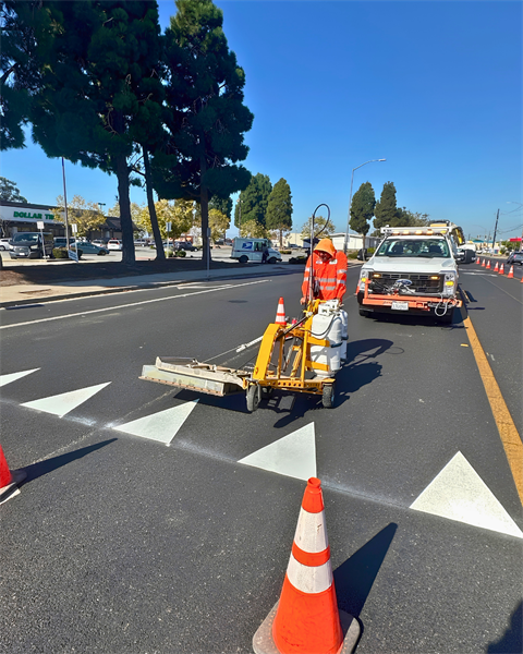 Person in a high visibility vest using machine to place thermo striping on road