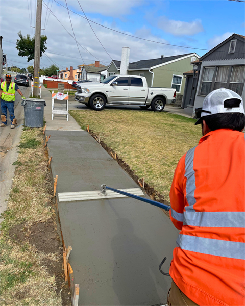 Person in a high visibility vest using a tool to flatten freshly paved sidewalk