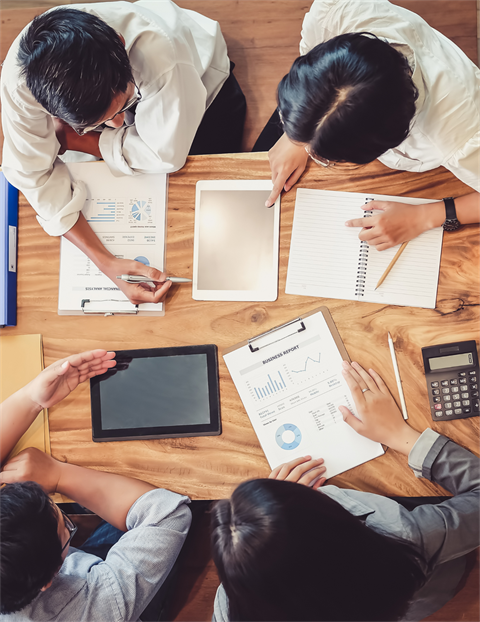 A group of people in a table discussing about a project with their devices and notepads.