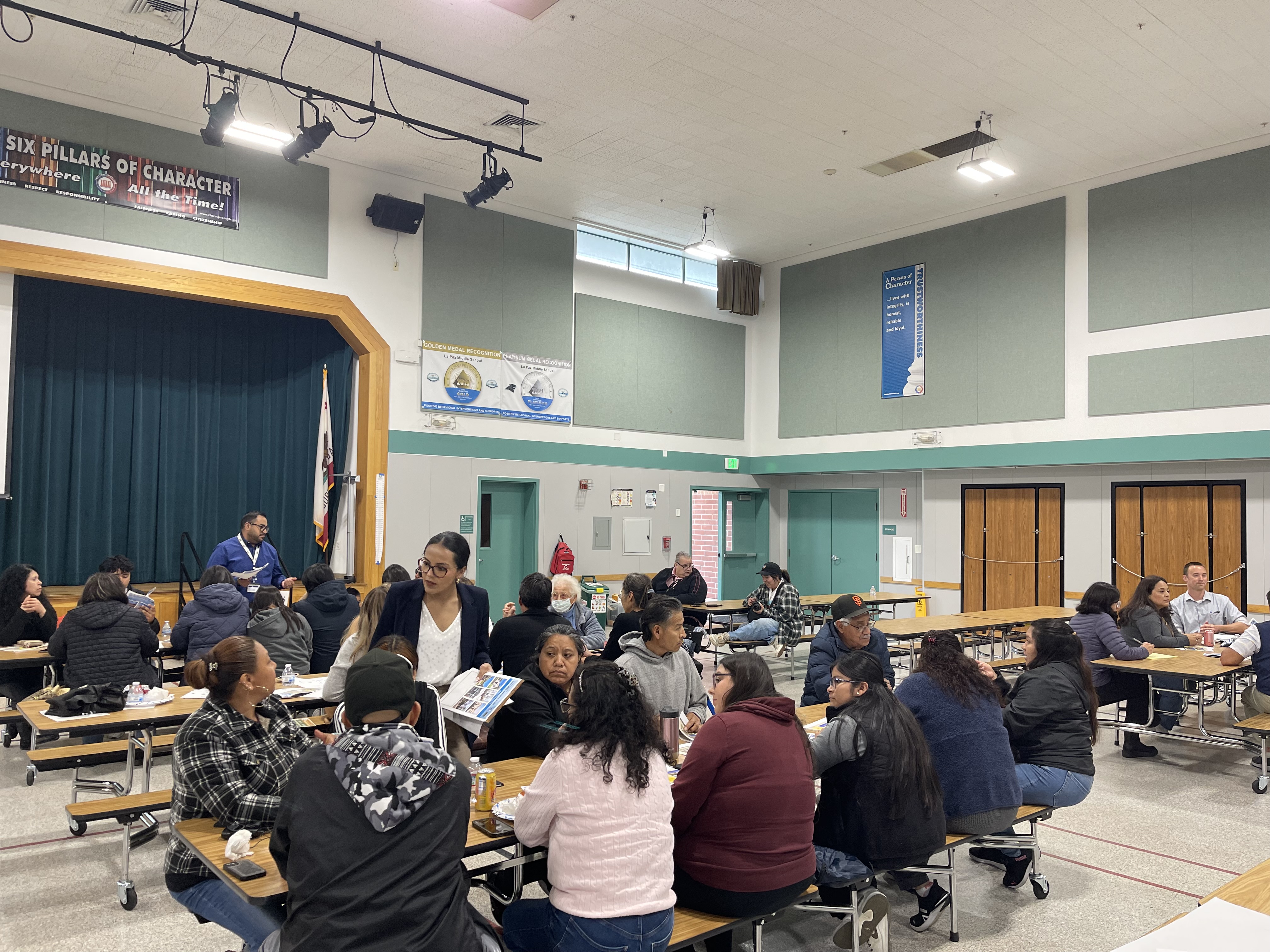Residents participating in a community workshop discussion at tables inside a meeting hall.