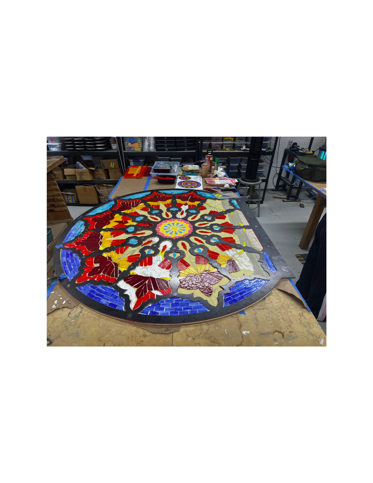 A round table covered with a colorful mosaic map made of small cut tiles, surrounded by craft supplies and boxes in a workshop.