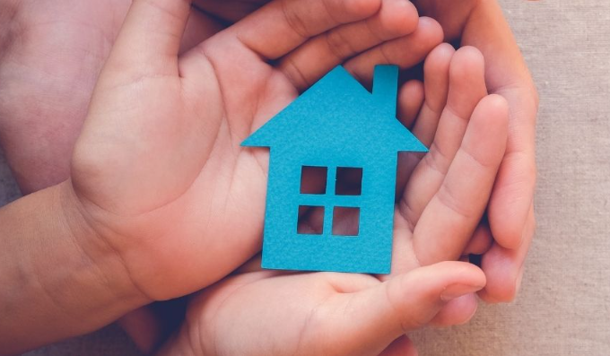 Close-up of hands holding a small blue house cutout symbolizing housing security and protection.