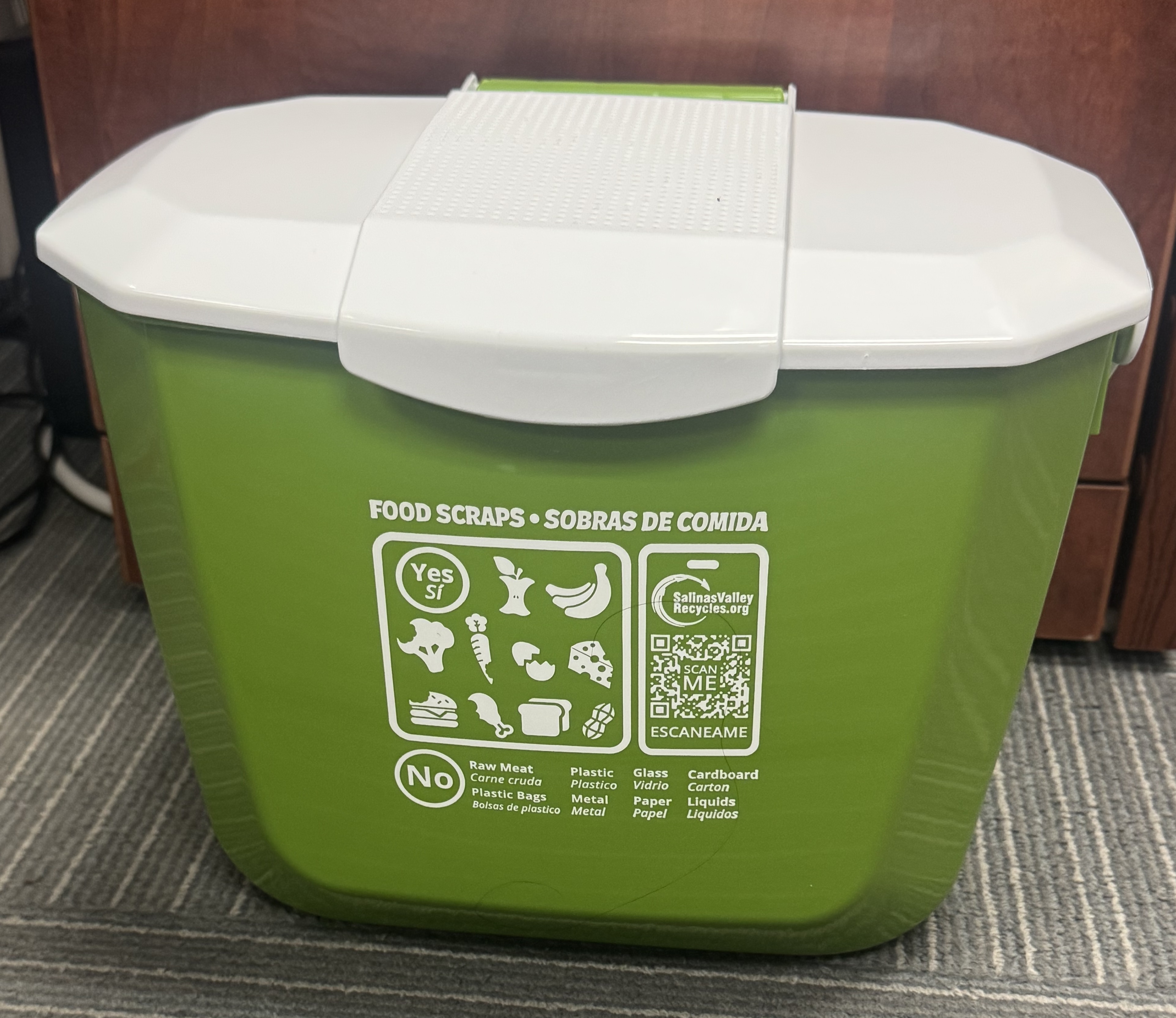 A green Salinas Valley Recycles food scrap bin with a white lid. Bilingual English and Spanish icons illustrate 